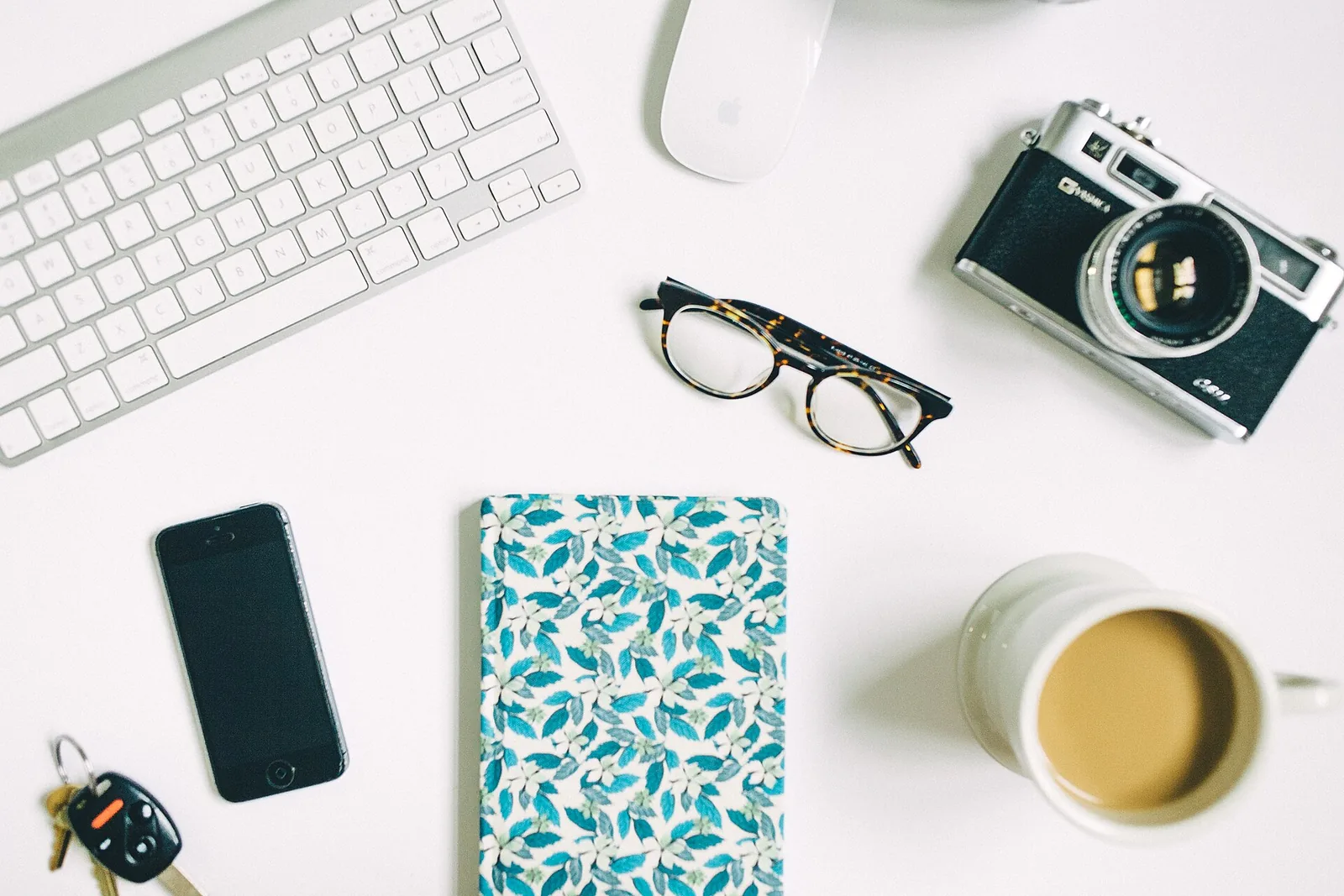 A notebook, keys, camera and coffee on a table, suggesting planning a property purchase