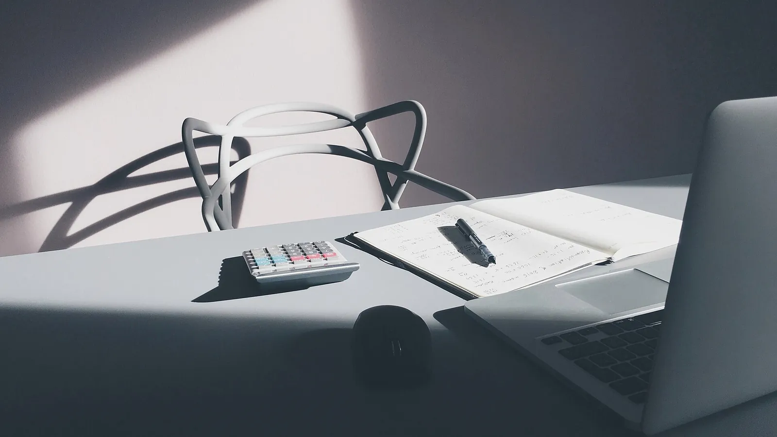 Desk with a laptop, calculator and papers in soft daylight